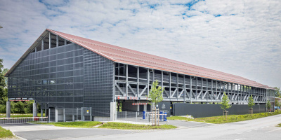 Die Anforderungen des Bauherrn ergaben ein außergewöhnliches Systemparkhaus. Zum einen bestand der Wunsch in der Ebene 0 möglichst viele Stellplätze für LKW-Züge unterzubringen. Zum anderen forderte der Bebauungsplan ein Satteldach.